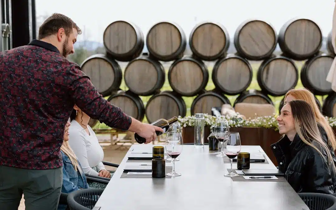 pouring wine at a table in front of barrels