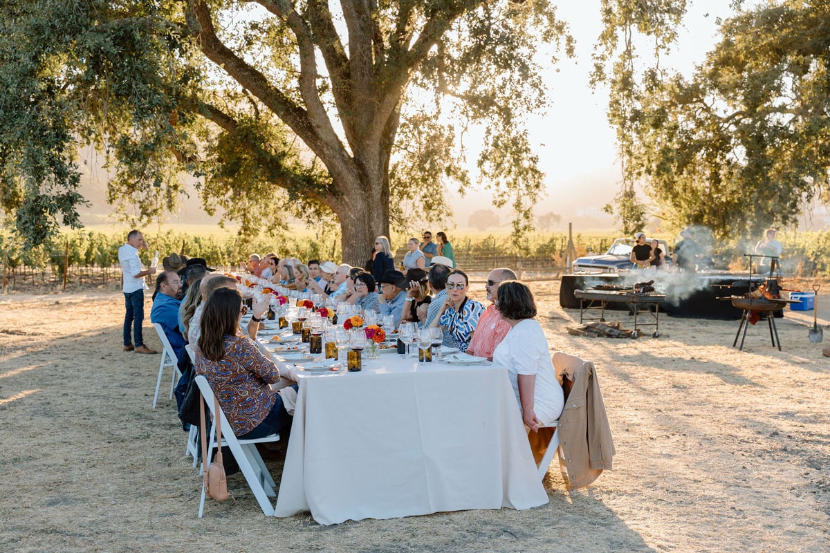 Guests enjoy Tomatoville farm-to-table dinner under oak trees at Hill Family Estate in Napa Valley vineyard setting.